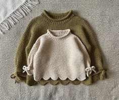 two knitted sweaters sitting on top of a bed next to a white pillow