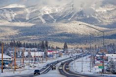 a road with snow covered mountains in the background and cars driving on it's side