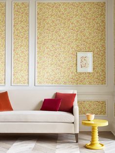 a white couch sitting next to a yellow table in front of two paintings on the wall