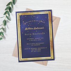 a blue and gold birthday party card on top of a wooden table with greenery