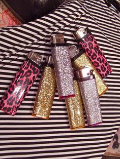 four lighters are laying on top of a black and white striped tablecloth with pink, gold, and silver designs