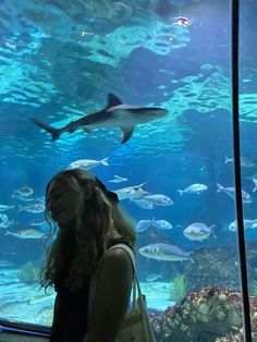 a woman standing in front of a large aquarium filled with lots of different types of fish