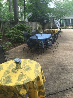 a patio with tables and chairs covered in yellow tablecloths, surrounded by trees