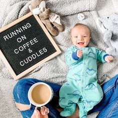 a baby sitting on the floor next to a coffee cup and stuffed animals with a sign that says running on coffee cuddles