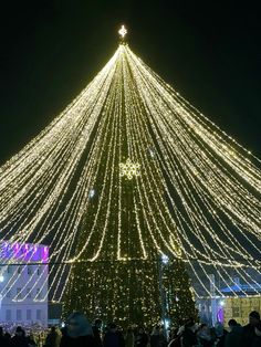 a large christmas tree is lit up in the night sky with hundreds of lights all around it