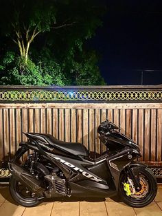 a black motorcycle parked in front of a wooden fence at night with its lights on