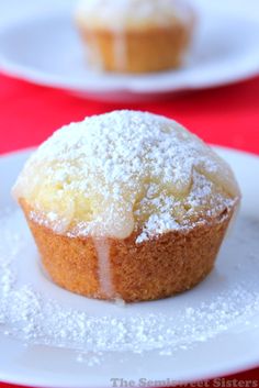 a muffin on a white plate with powdered sugar and red table cloth in the background