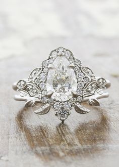 an oval shaped diamond ring with leaves and diamonds on the band, set in 18k white gold