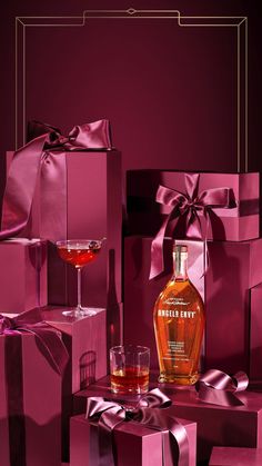 a bottle of whiskey sitting next to two glasses and boxes with pink bows on them