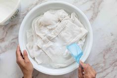 two hands reaching for something in a bowl that is filled with white cloth and water