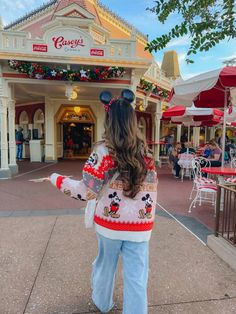 a woman standing in front of a building with mickey mouse ears on her head and arms out