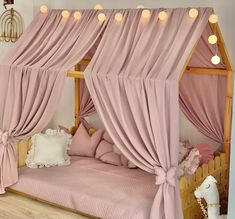 a canopy bed with pink drapes and pillows on the bottom, in a girls bedroom