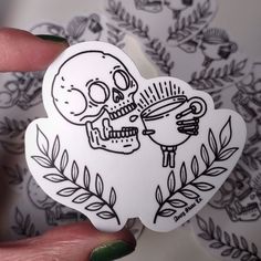 a hand holding a sticker with a skull and cup on it's side