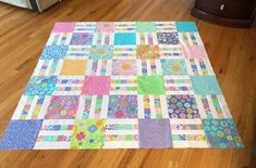 a colorful quilt is laying on the floor in front of a dresser and table top