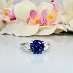 a blue and white diamond ring sitting on top of a table next to orchids