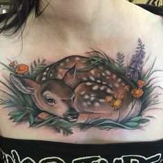 a woman's chest with a deer tattoo on it and flowers around the neck