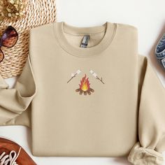 a sweater with a fire and two arrows on it sitting next to some shoes, straw hat and sunglasses