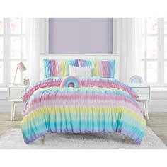 a rainbow colored bed in a bedroom next to a white dresser and window with curtains