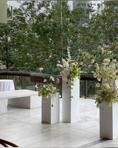 four white vases with flowers in them sitting on the ground near tables and benches