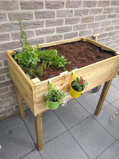 a wooden planter filled with plants on top of a patio next to a brick wall