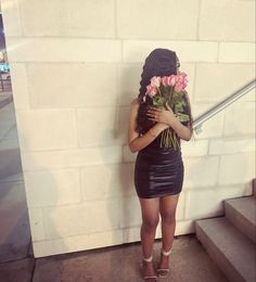 a woman with flowers on her head standing next to a wall holding a bunch of roses