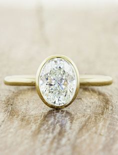 a close up of a diamond ring on a wooden surface with the center stone missing