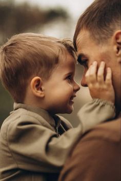 a man holding a little boy in his arms and looking at each other's eyes