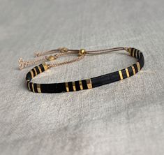 Beautiful elegant bracelet made with silk cord and Japanese Tila Miyuki beads. The classic combination of black & gold will never go out of Fashion ! These bracelets are adjustable by using the sliding bead and are easy to stack with your other favorite bracelets. S I Z E : * Bracelet opens up to 24 cm and nearly always fits, it has to be shoven over your hand and is adjustable by using the sliding bead M A T E R I A L * Beie silk cord 0.8 mm . * Miyuki Tila beads ( 5 mm), black & gold ( 24 cara Cord Bead Bracelet, Tila Tile Bracelets, Miyuki Tila Beads, Square Bead Bracelet, Black And Gold Beaded Bracelets, Tila Bead Jewelry, Tila Bead Bracelets Tutorials, Miyuki Tila Bracelet, Bracelet Tila