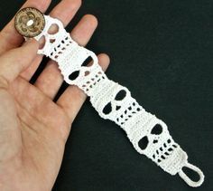 a hand is holding a white crochet bracelet with a button on it's end