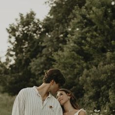 a man and woman standing next to each other in front of some trees on a sunny day