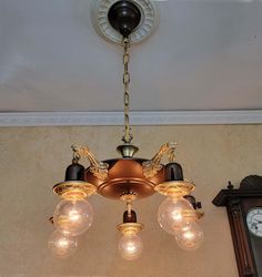 a chandelier hanging from the ceiling with three light bulbs on it and a clock in the background