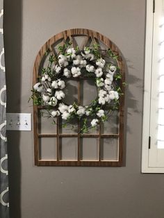 a wreath is hanging on the wall next to a window with cotton flowers in it