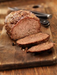 a loaf of meat sitting on top of a wooden cutting board next to a knife