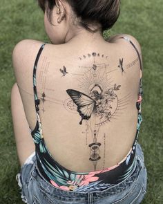 a woman with a butterfly tattoo on her back is sitting in the grass and looking down