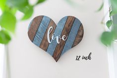 a wooden heart with the word love painted on it next to some green leaves in front of a white wall