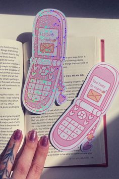 a woman's hand is holding an open book with stickers on it and the pages are pink