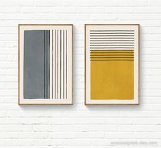 two framed art pieces on a white brick wall, one with grey and yellow lines