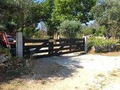 a tractor is parked behind a gate in the dirt near some trees and bushes on a sunny day