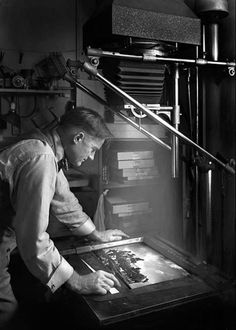 a black and white photo of a man looking at pictures on a table in front of a lamp