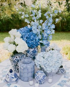 blue and white flowers are in vases on a table with other items around it