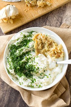 a white bowl filled with mashed potatoes and parsley on top of a wooden cutting board