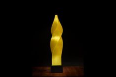 a yellow sculpture is on display in the dark, it looks like an abstract piece of art