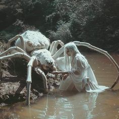 a woman in white dress standing next to a giant spider on top of a body of water