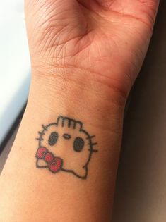 a hello kitty tattoo on the wrist of a woman's hand with a bow