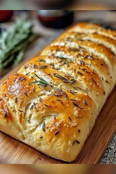 a loaf of bread sitting on top of a wooden cutting board next to some herbs