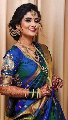 a woman in a blue and green sari with gold jewelry on her head, smiling at the camera