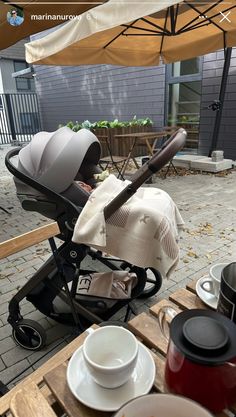 a baby in a stroller is sitting on a table with plates, cups and saucers