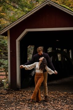 a man and woman are dancing in front of a covered bridge during their fall engagement session