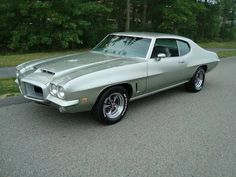 an old muscle car is parked on the side of the road in front of some trees