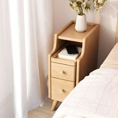 a wooden nightstand with flowers on it next to a bed and white curtains in a bedroom